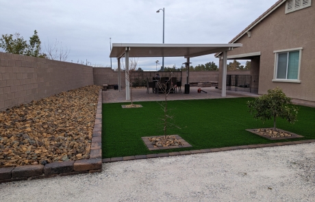 artificial-turf-backyard-with-covered-patio.jpg Backyard with artificial turf, stone edging, and a covered patio seating area.