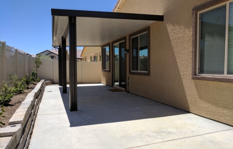 backyard-covered-patio-with-stone-retaining-wall.jpg Backyard with concrete patio, covered shade structure, and stone retaining wall along fence line.