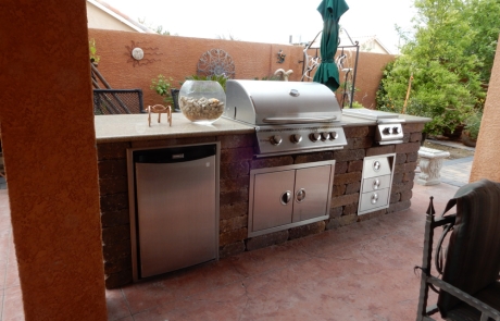 outdoor-kitchen-with-stone-island-and-grill.jpg Covered patio outdoor kitchen with stone island, stainless steel grill, and fridge.