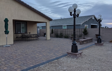 stone-patio-firepit-with-lamp-posts.jpg Stone patio with built-in firepit and decorative lamp posts in landscaped backyard.