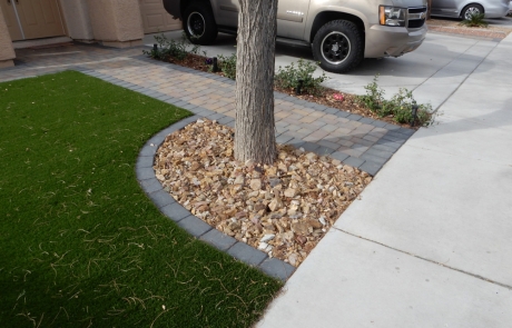 tree-ring-landscape-with-pavers-and-rocks.jpg Artificial turf front yard with tree surrounded by stone edging and pavers.
